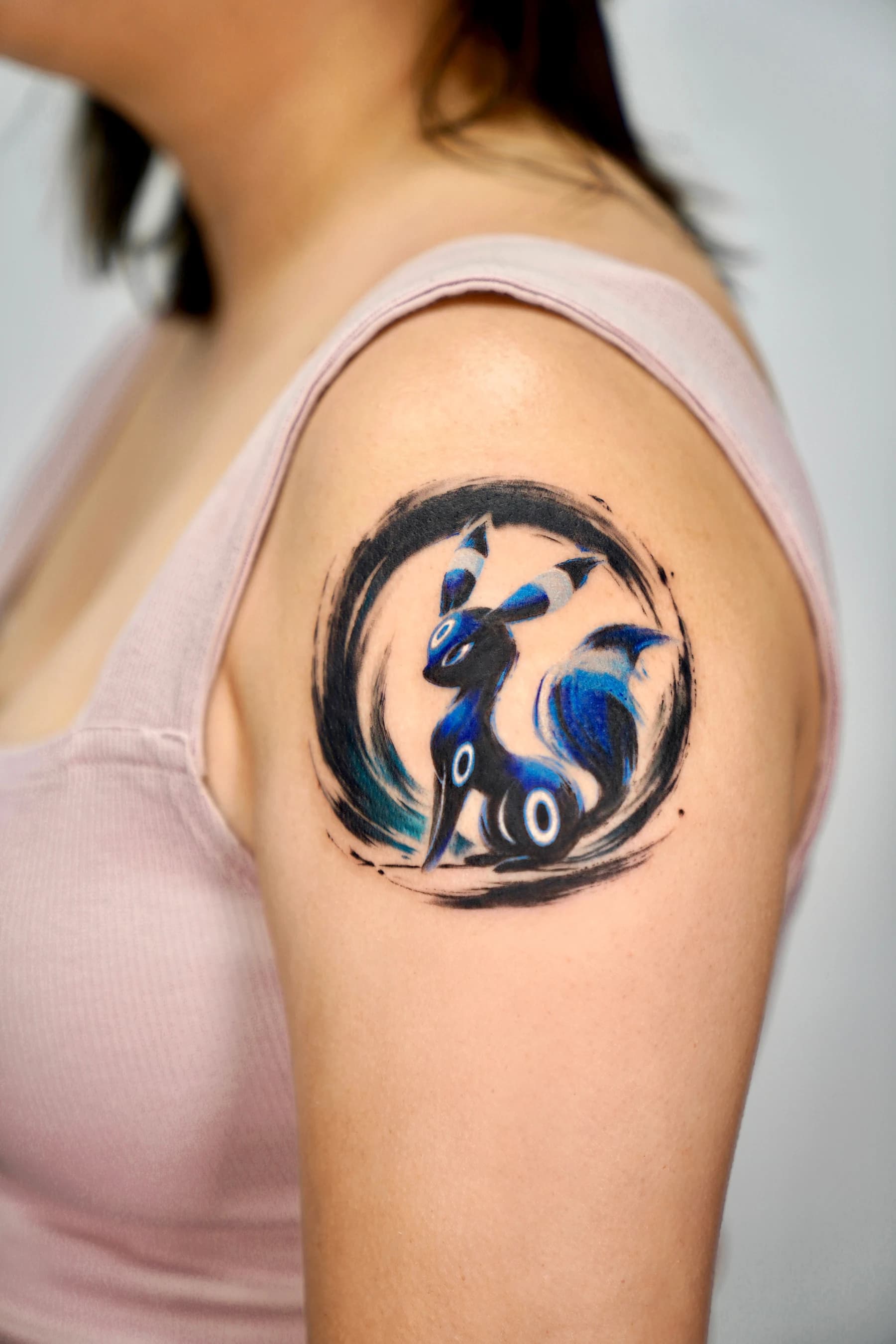 Ink brushstroke Umbreon tattoo on the upper arm with glowing moonlit rings